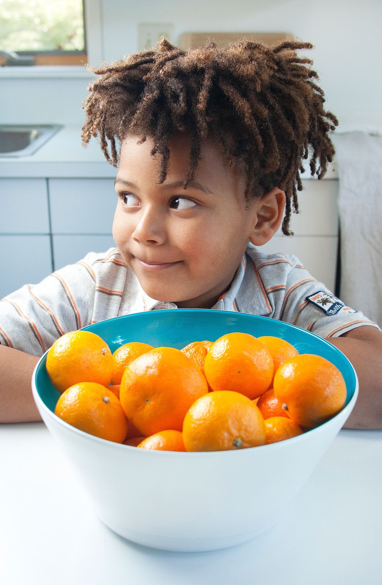 An African-American boy smiles in front of a a teal blue handblown glass bowl filled with clementines. Made in the USA from Serve Kindness.